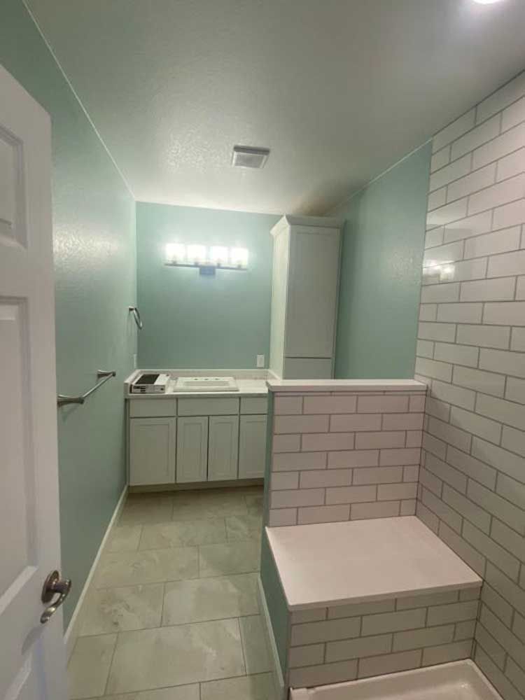 Bathroom with light blue walls, white cabinets, and subway tile shower.
