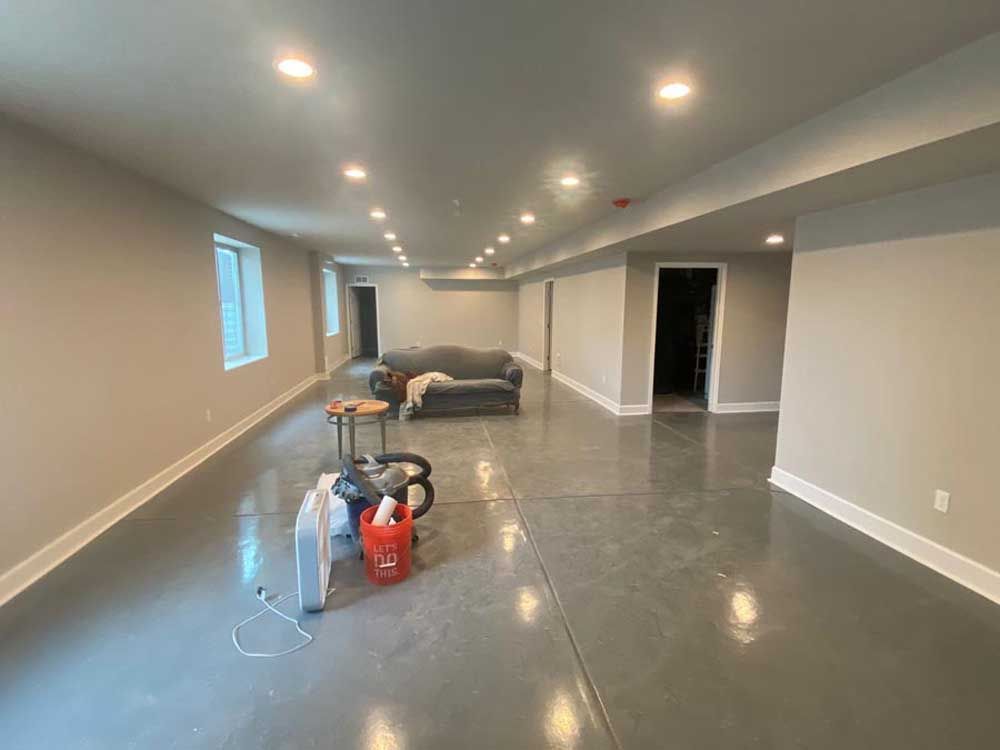 A long, gray-floored basement with recessed lights, a gray sofa, and some items on the floor.