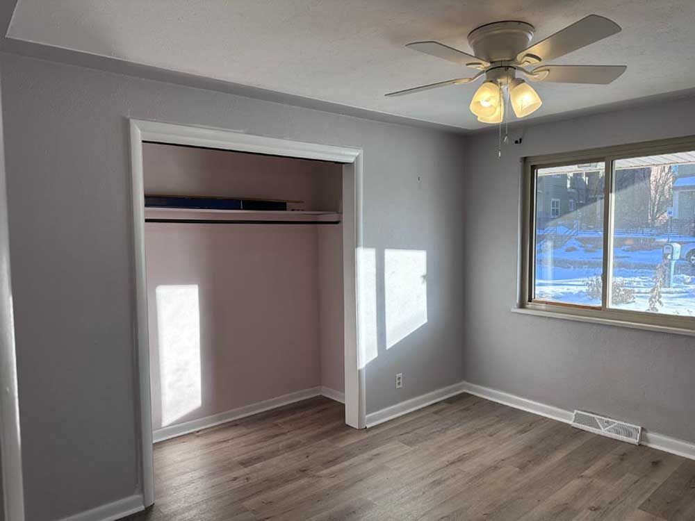 Bedroom with grey walls, white trim, a closet, window, ceiling fan, and wood-look flooring.