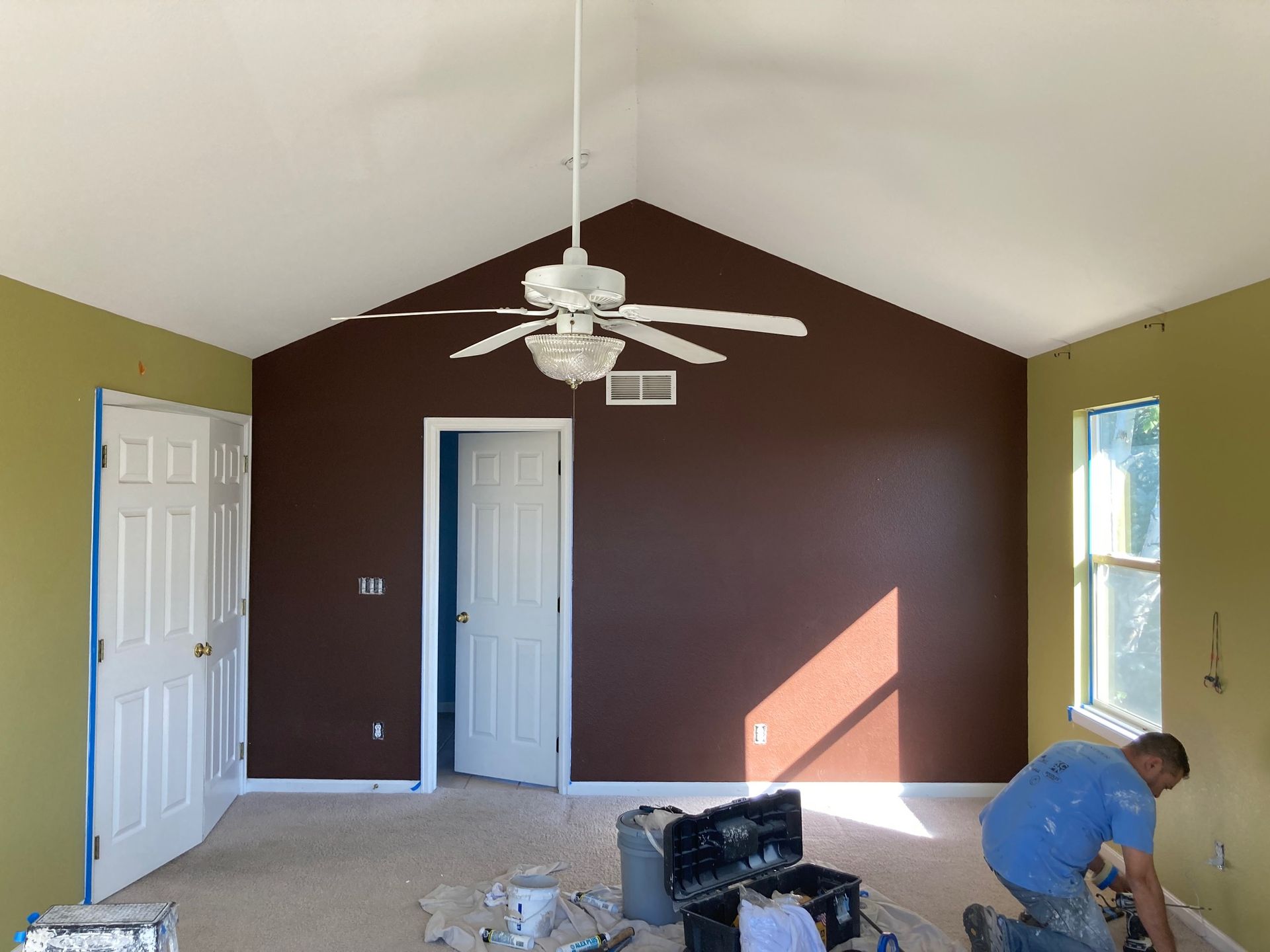 Room interior with brown and green walls, white ceiling, and a worker painting the wall.