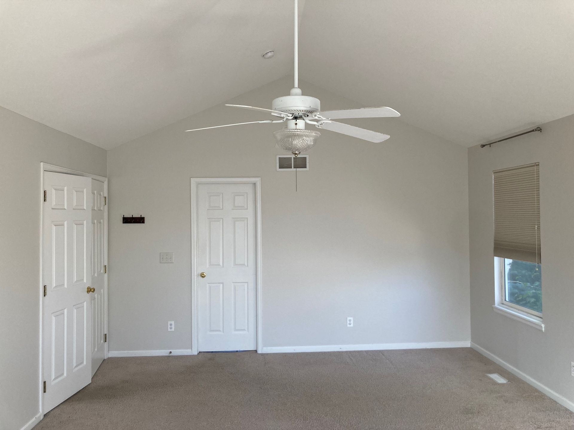 Bedroom with sloped ceiling, white doors, and a ceiling fan; carpeted floor and a window with a shade.