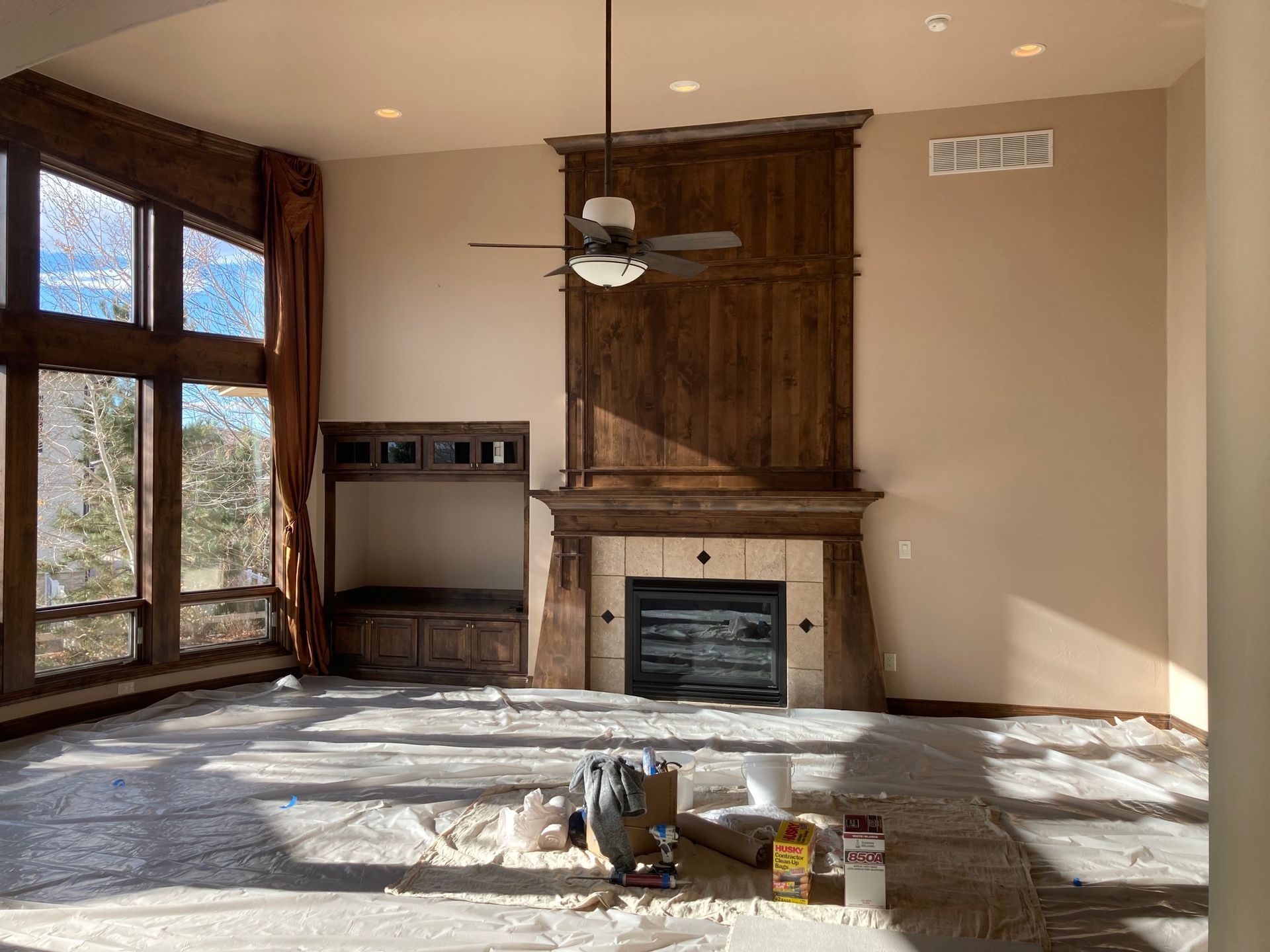 Empty living room with fireplace and large windows; construction materials on the floor.