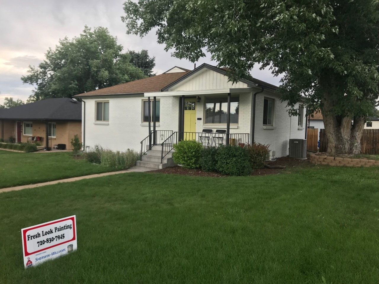 White house with yellow door, on a green lawn, for sale sign in front.
