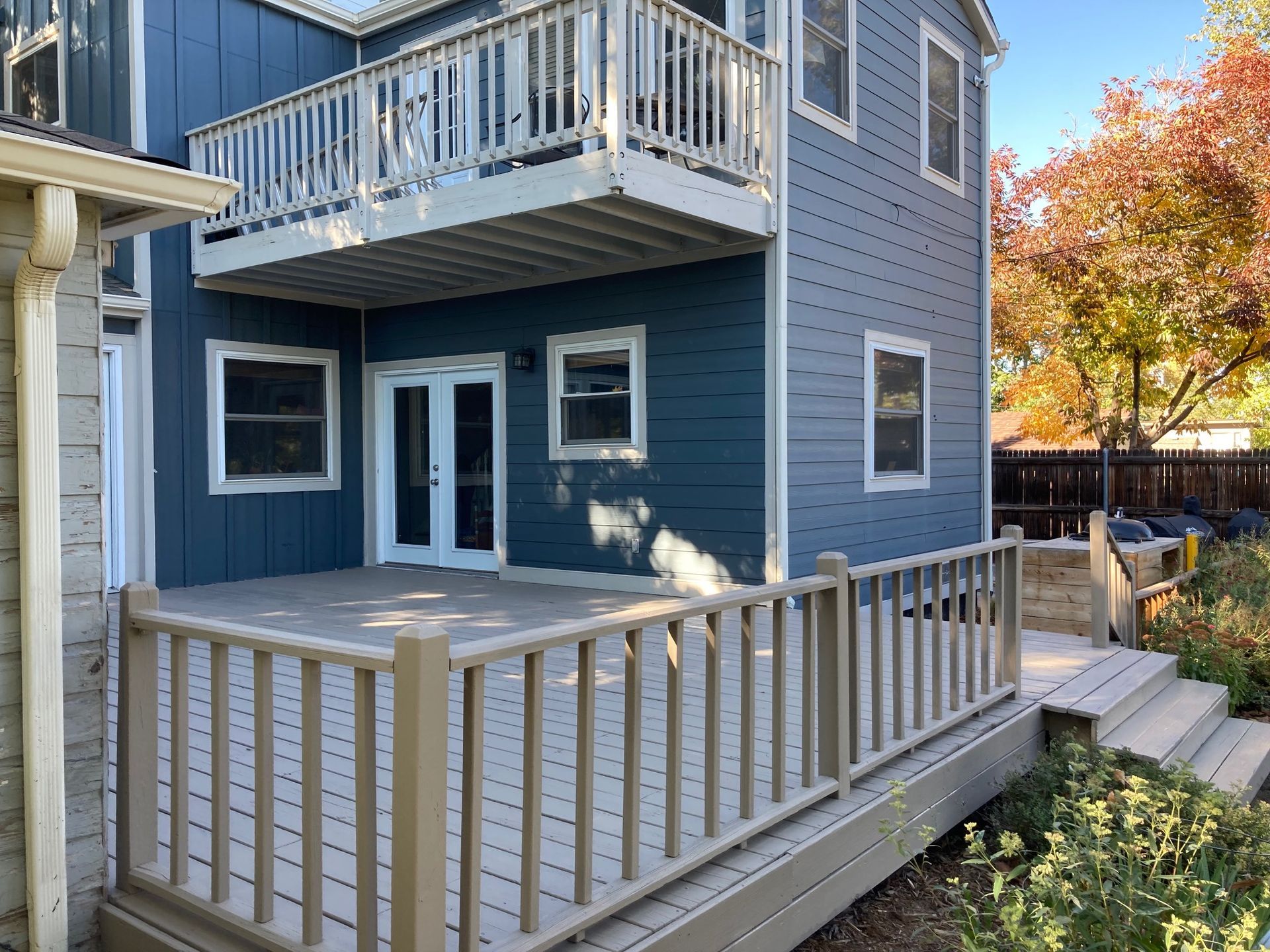 Blue house exterior with deck and balcony, featuring wooden railings and stairs.