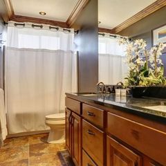Bathroom with wooden cabinets, dark countertop, white shower curtain, and a floral arrangement.