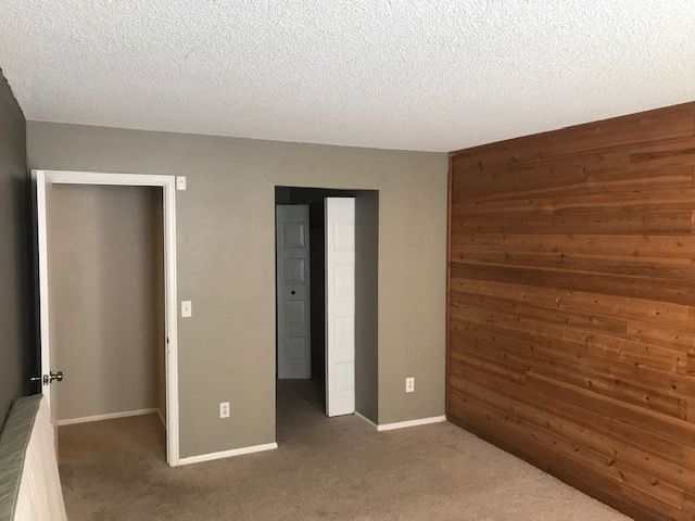 Empty room with wood-paneled wall, neutral-colored walls, and doorways.