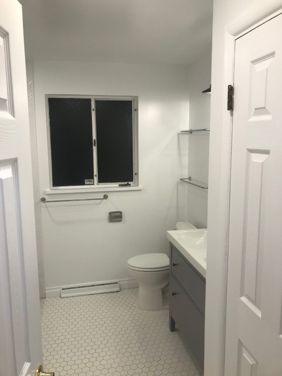 Bathroom with white walls, window, toilet, gray vanity, and hexagon tile floor.