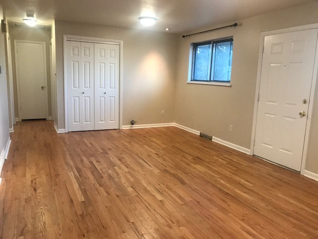 Empty room with hardwood floors, white doors and closet, a window, and beige walls.