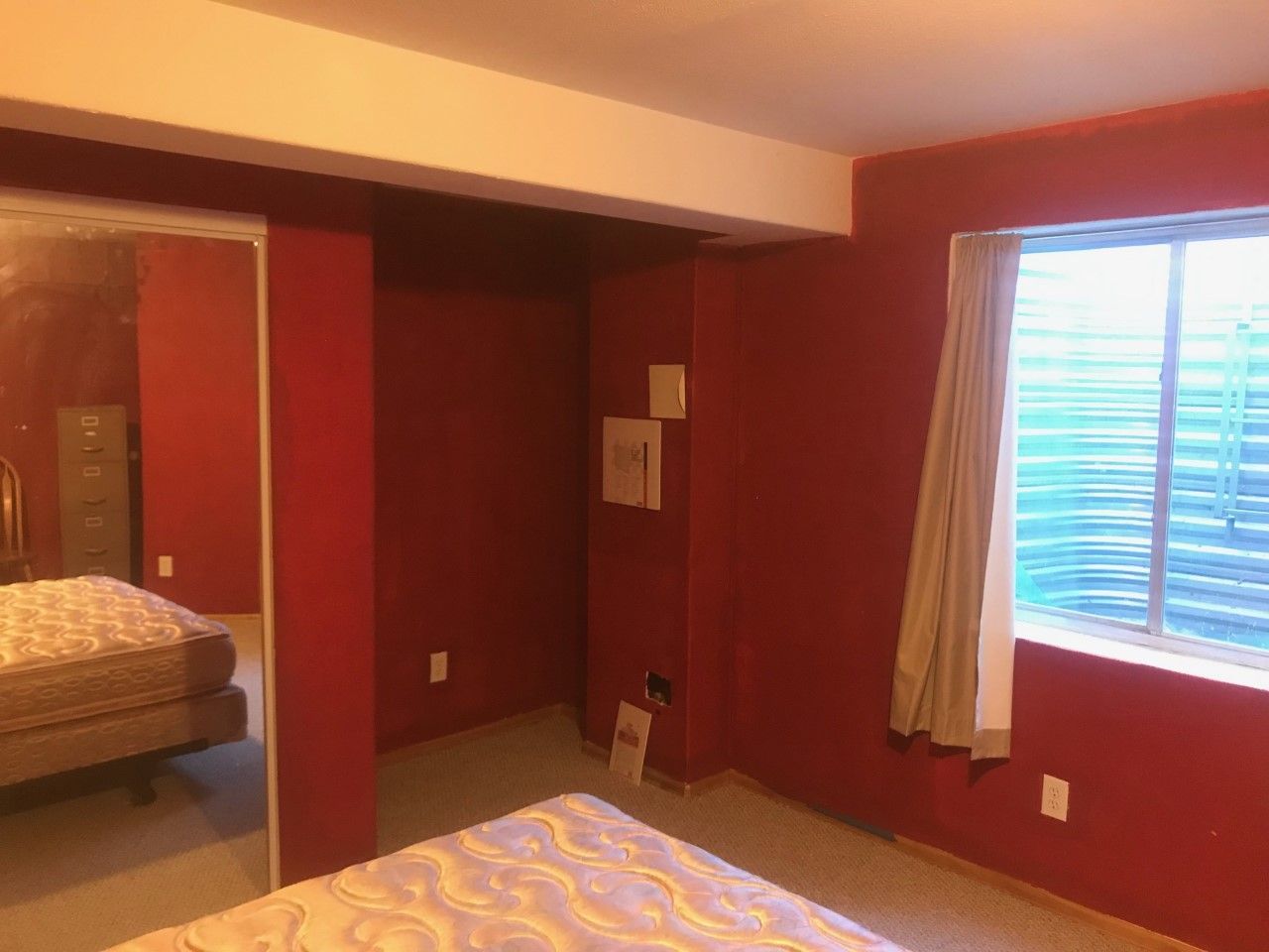 Red bedroom with a bed, mirror, window with blinds, and a built-in closet area.