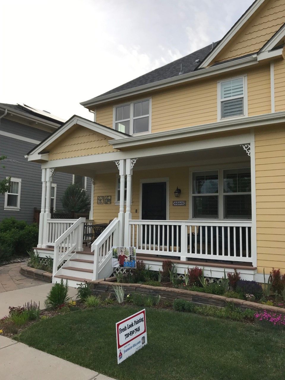 Yellow house with white porch and railings; small front yard with a tutoring sign.