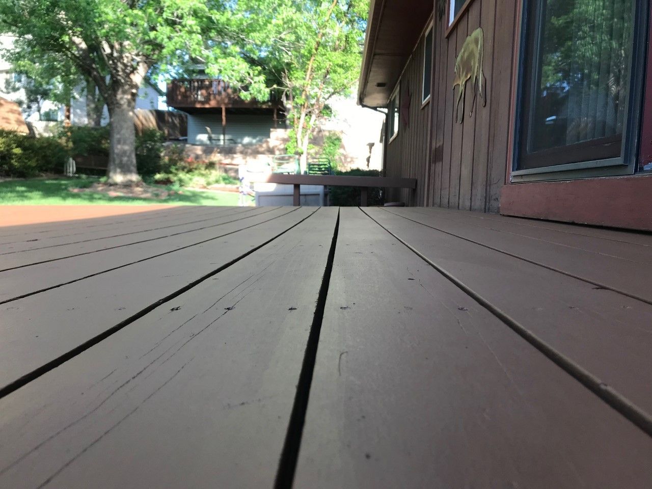 Wooden deck leading towards a house. Brown boards with cracks, sunny outdoor setting.