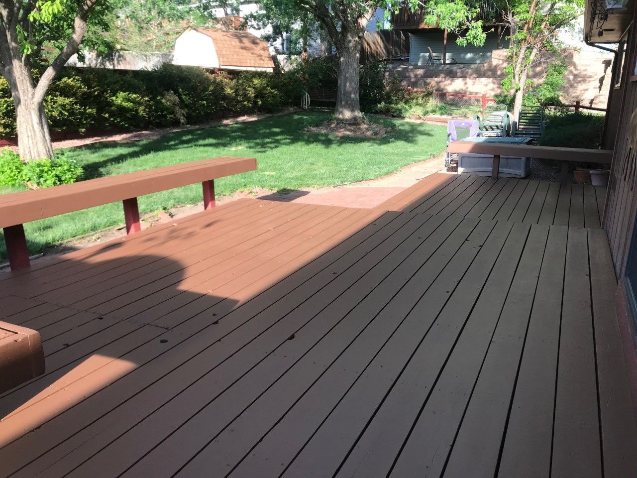 Brown wooden deck in backyard with grass and trees.