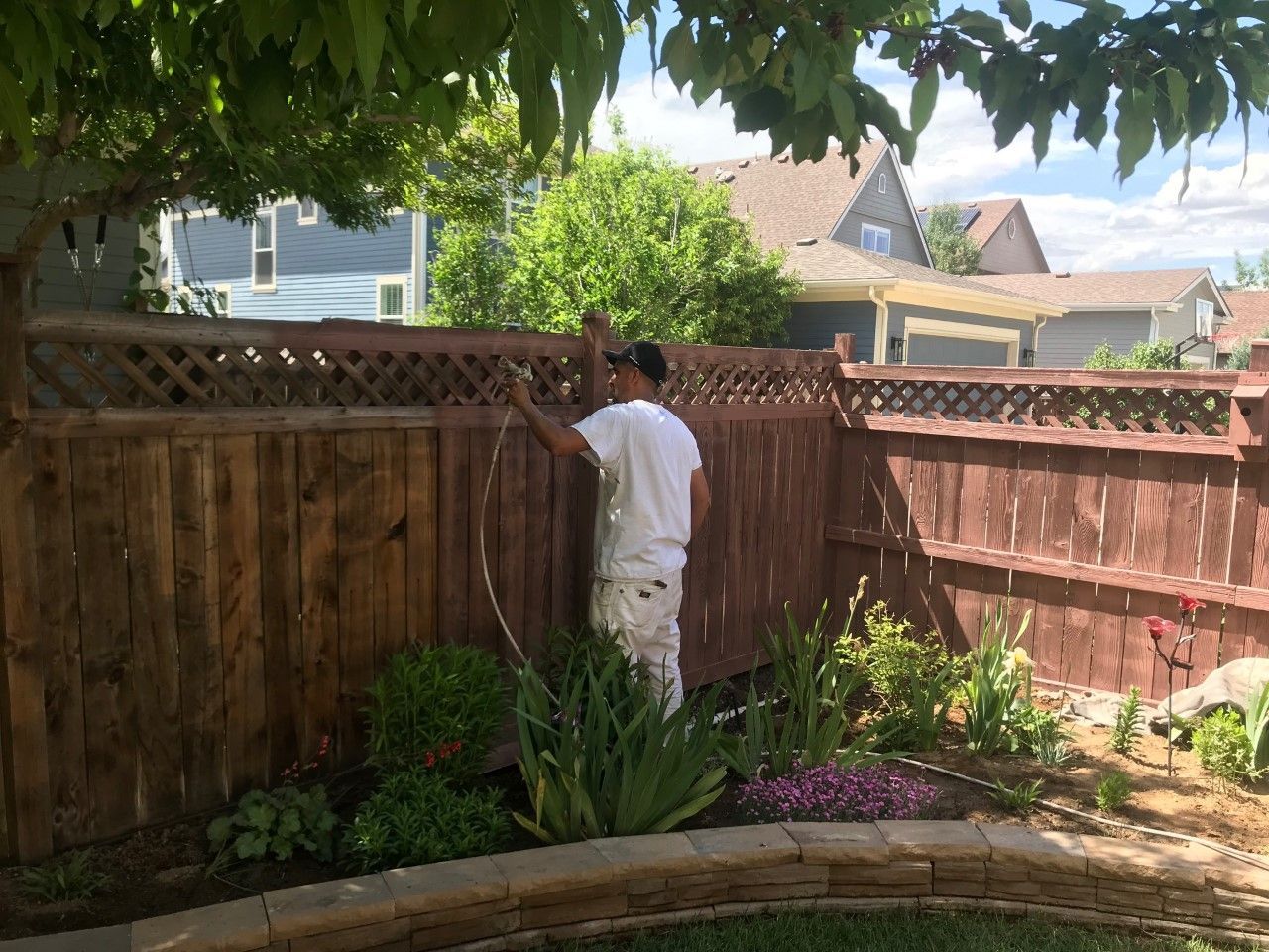 Person painting a brown wooden fence outdoors.