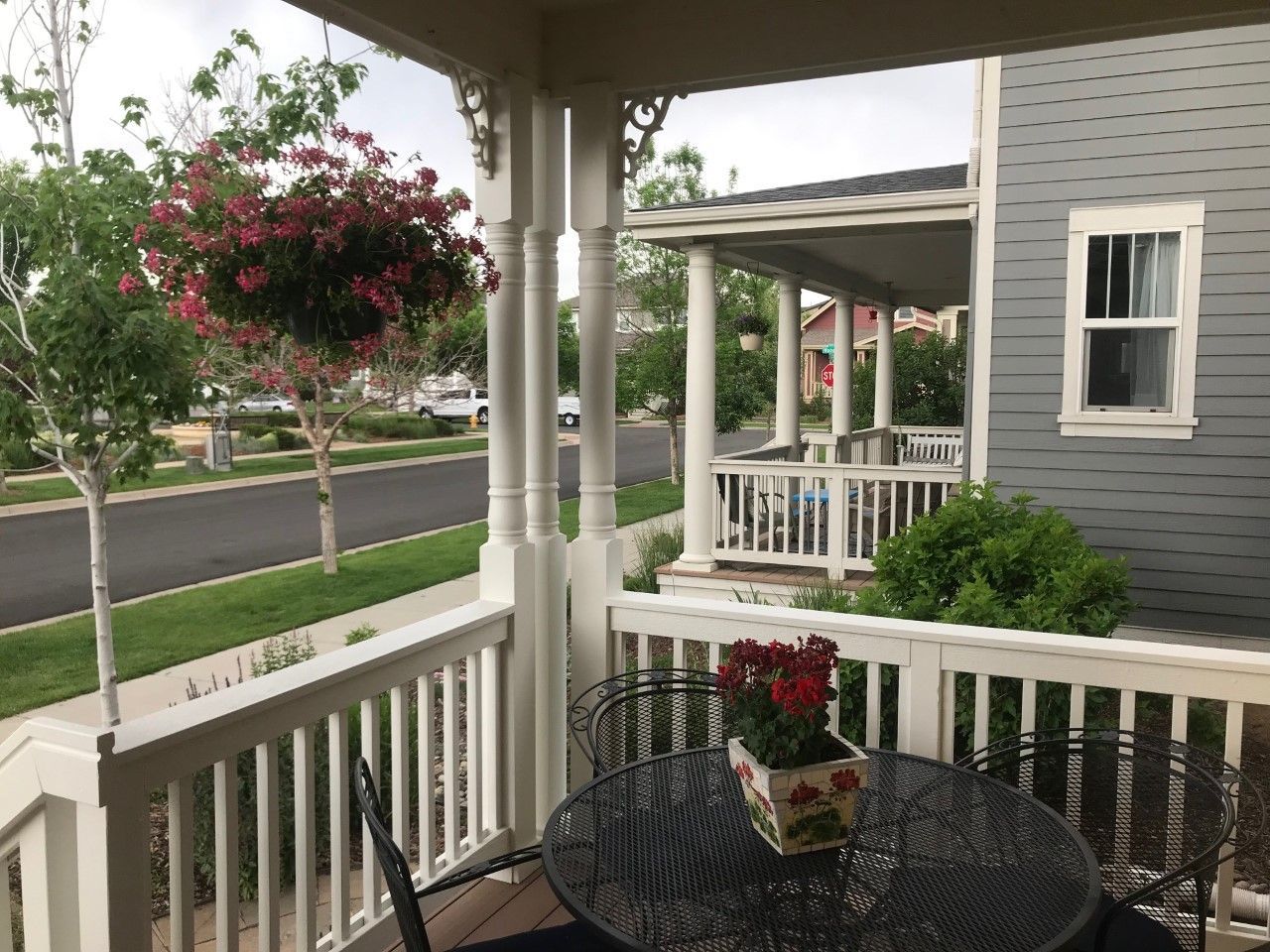 Porch view with a table and flower pot, street and houses visible.