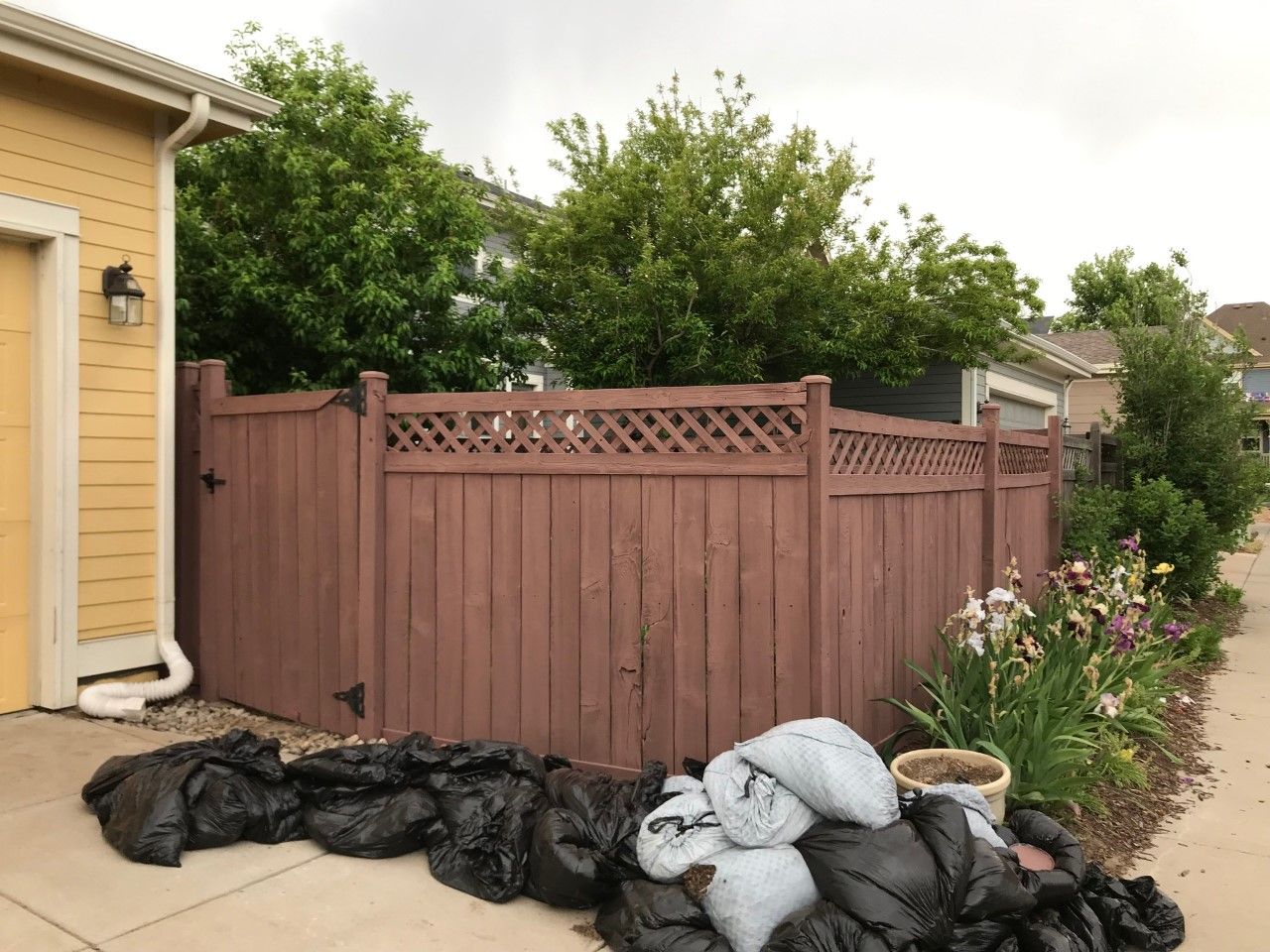 Brown wooden fence with lattice detail, next to a garage, with bags of debris in front.