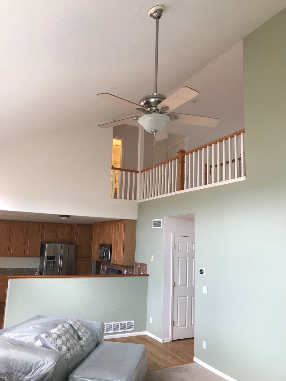 A room with high ceilings, a balcony, and a ceiling fan; painted in light green and white.