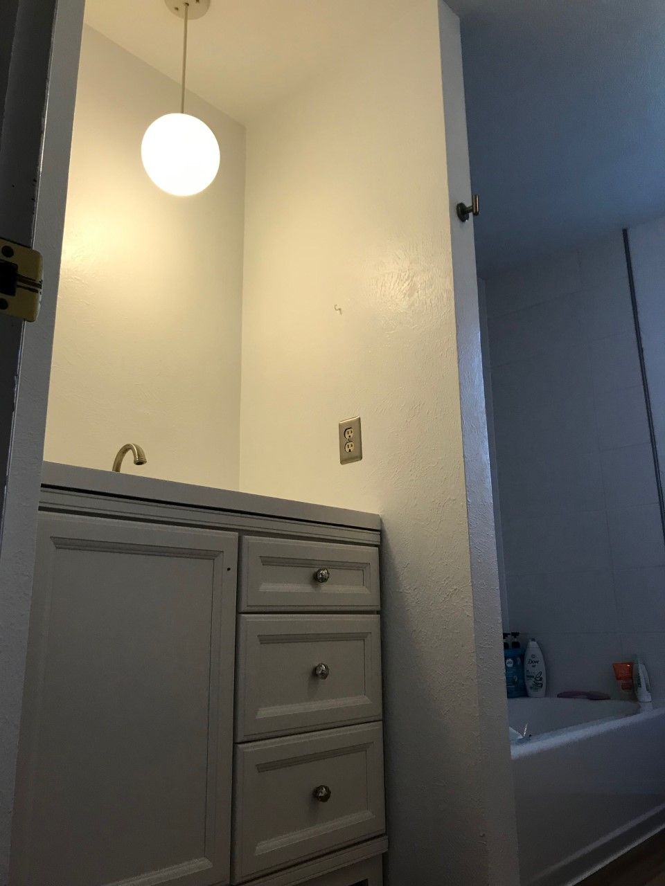 White bathroom with vanity and overhead globe light. Open doorway to a bathtub.