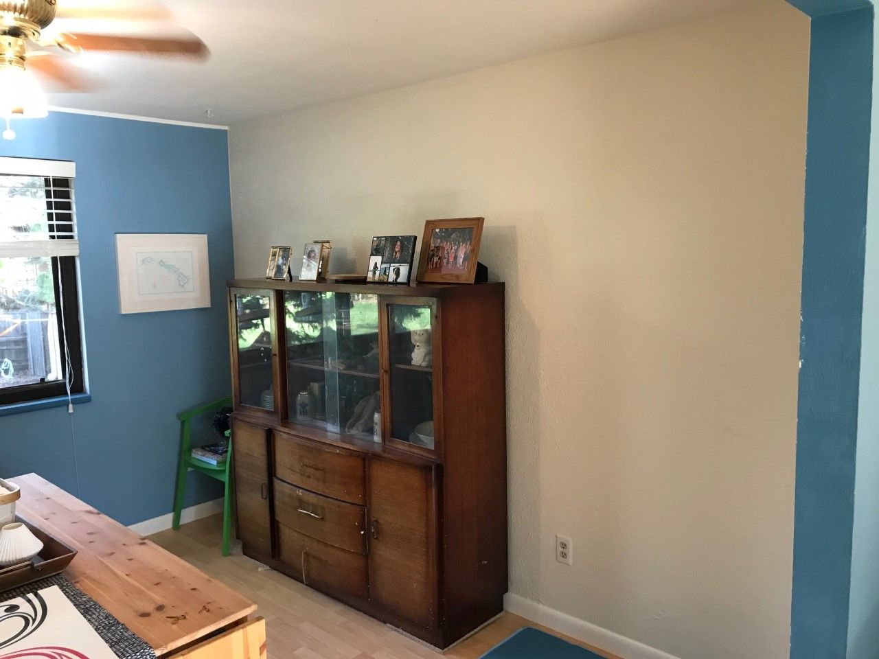 Dining room with wood hutch, blue and beige walls, window, and small table.