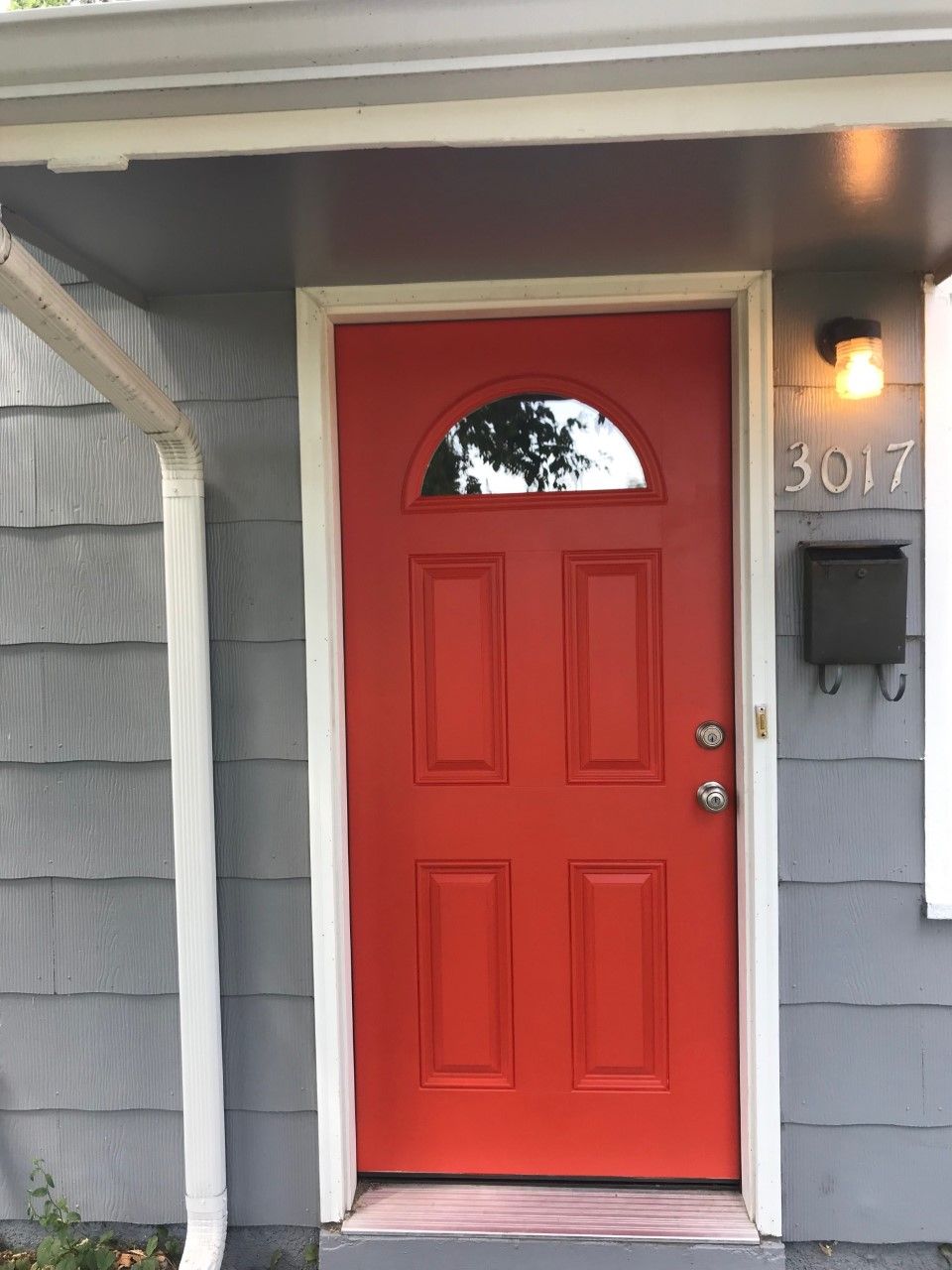 Red front door with arched window, gray siding, white trim, and a black mailbox.