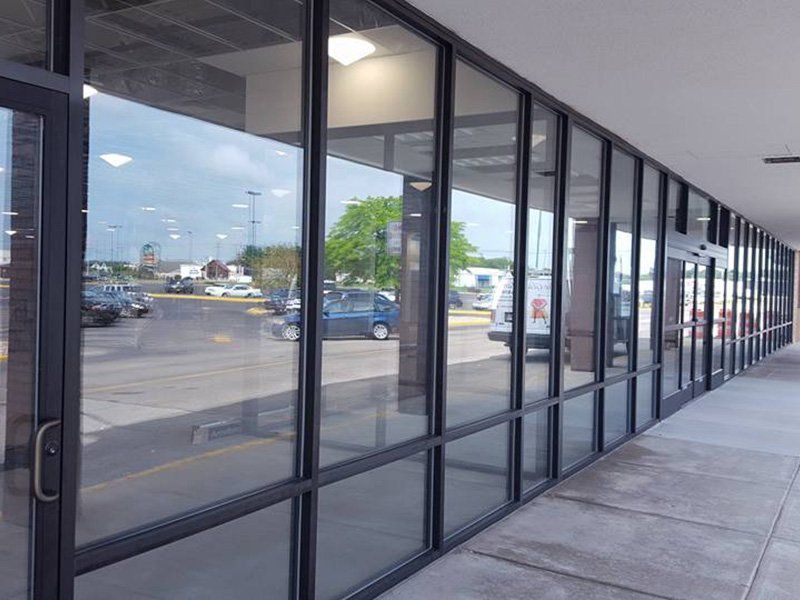 Empty storefront windows along a covered sidewalk in a shopping center, reflecting parked cars.