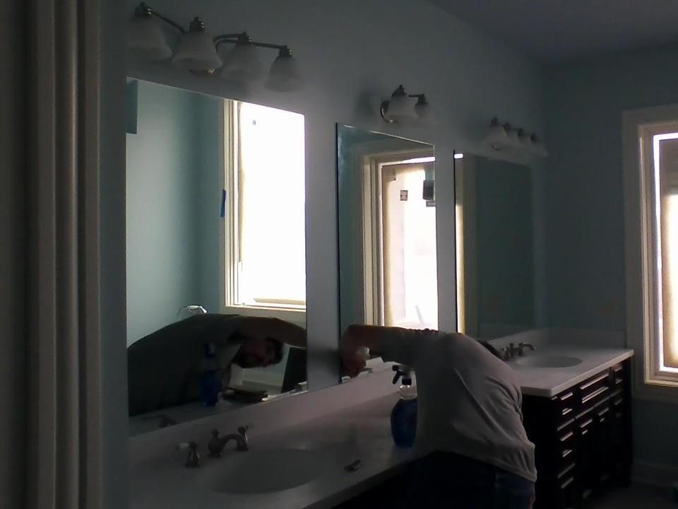 Person leaning over bathroom sink in a teal room with mirrors and wall lights