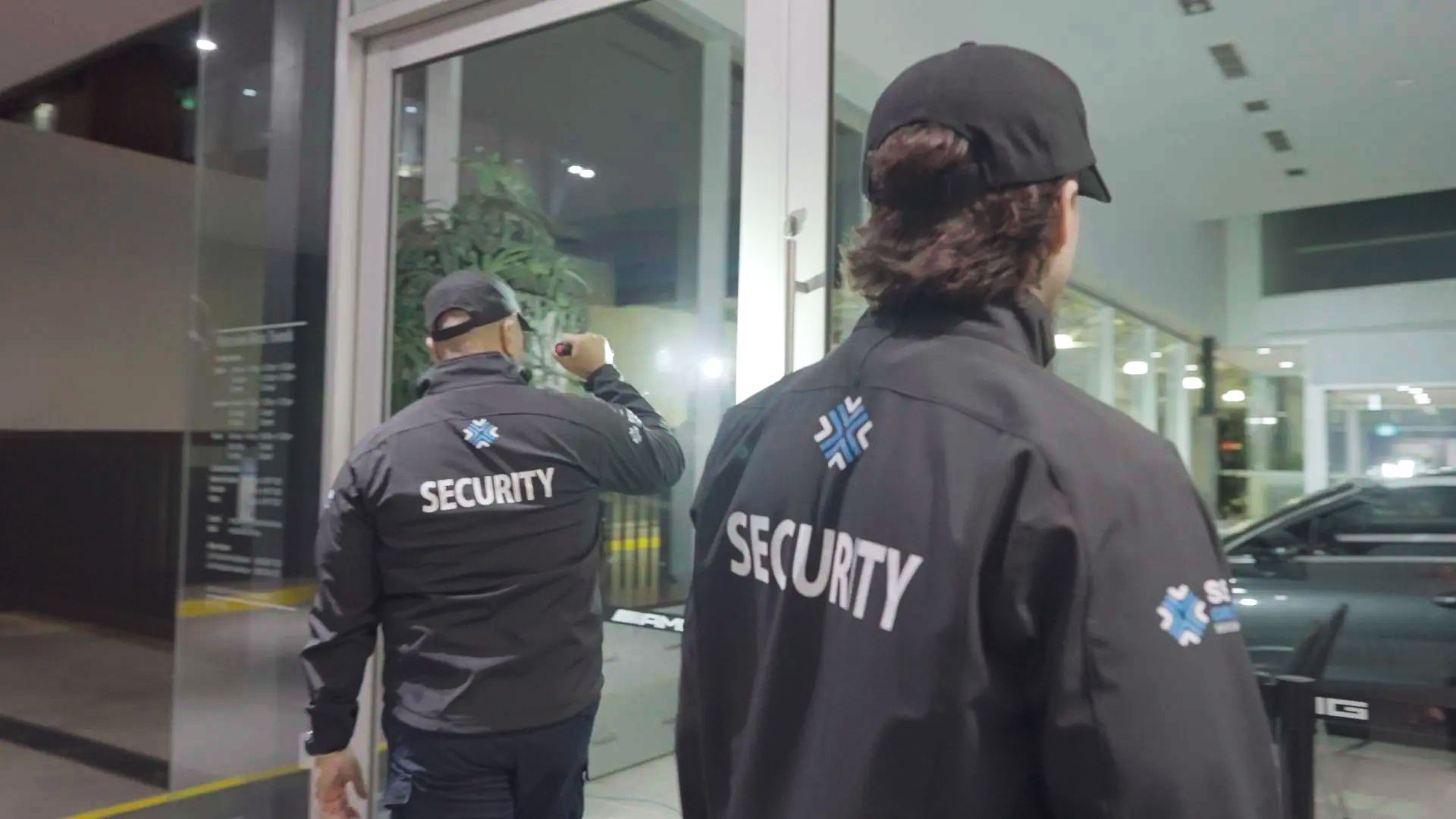 Two security guards are standing in front of a glass door.