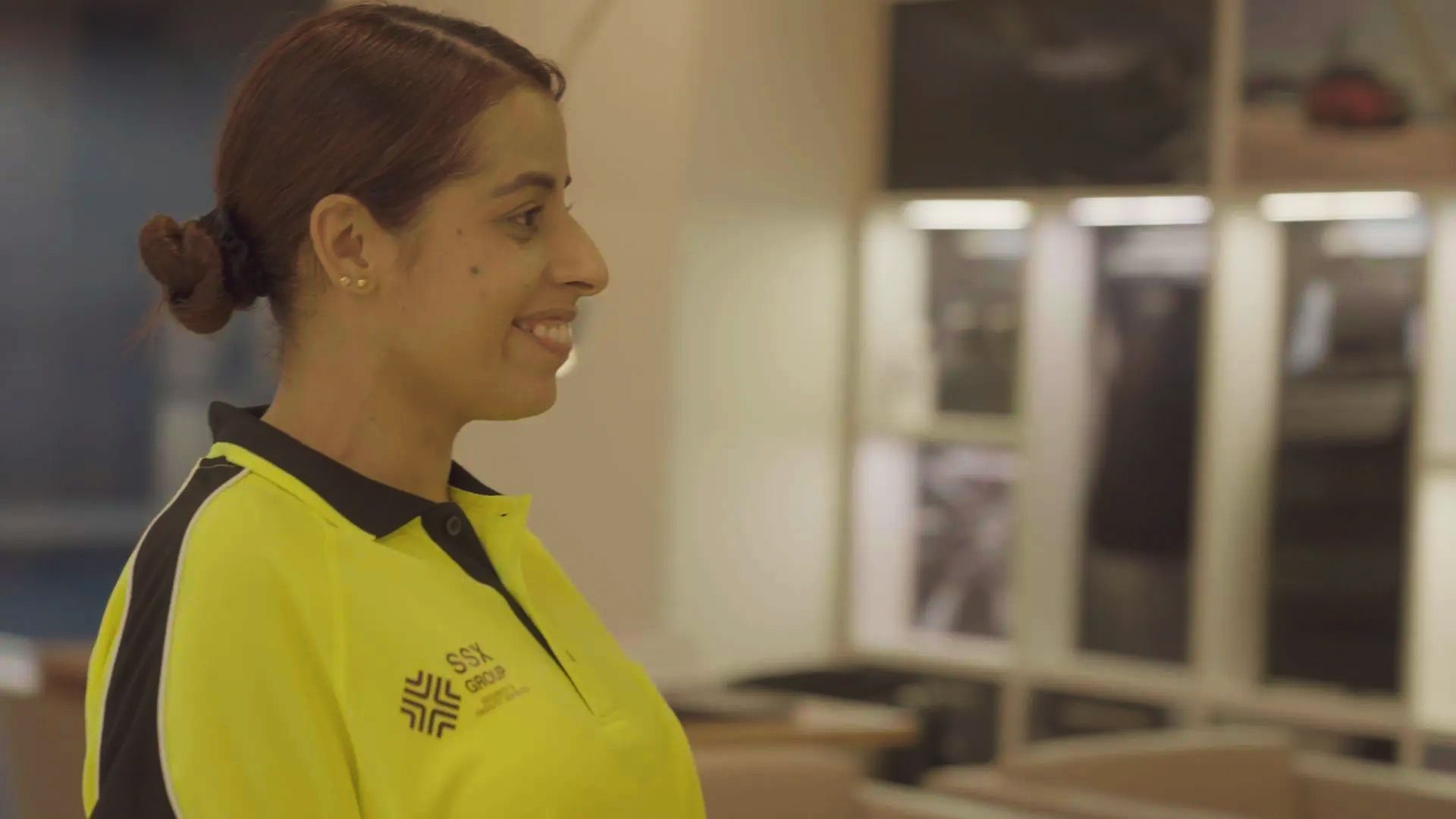 A woman in a yellow shirt is smiling in a room.