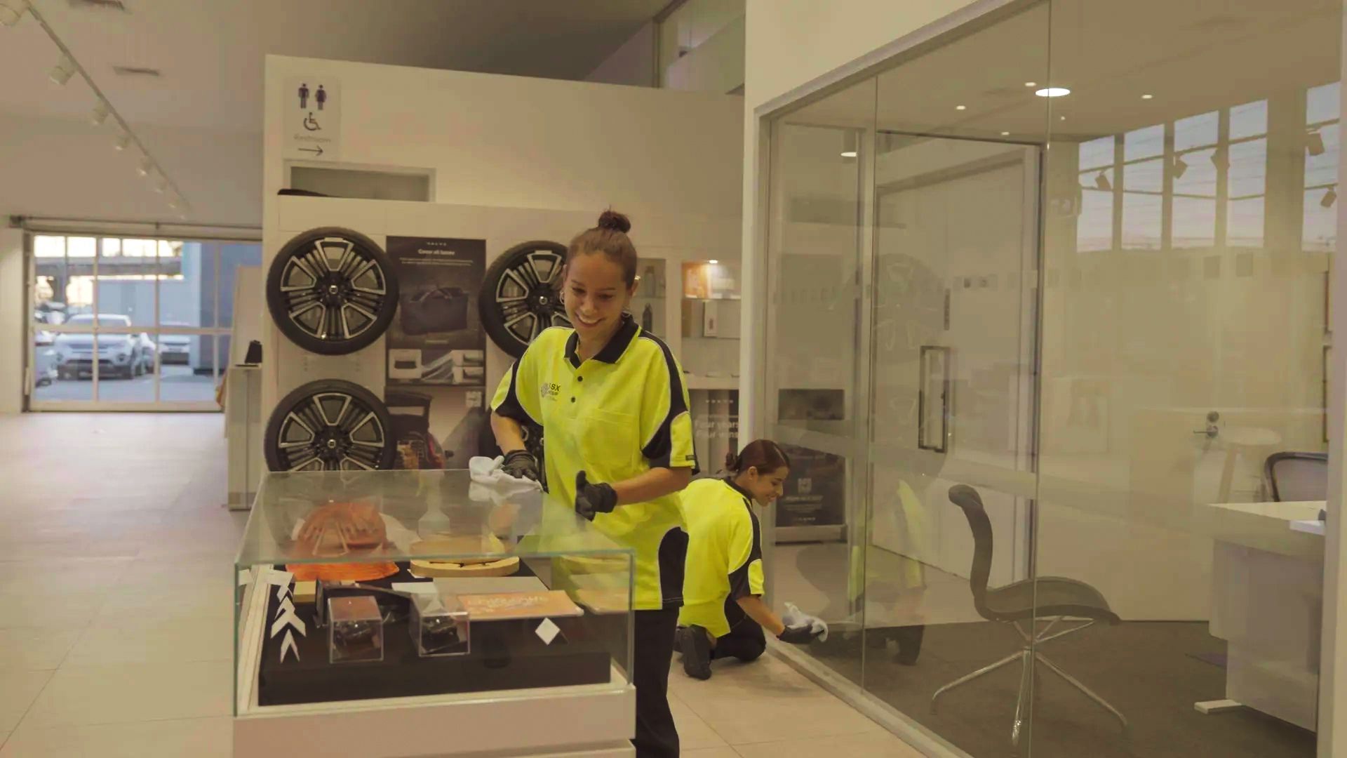 A woman in a yellow shirt is cleaning a glass table in a room.