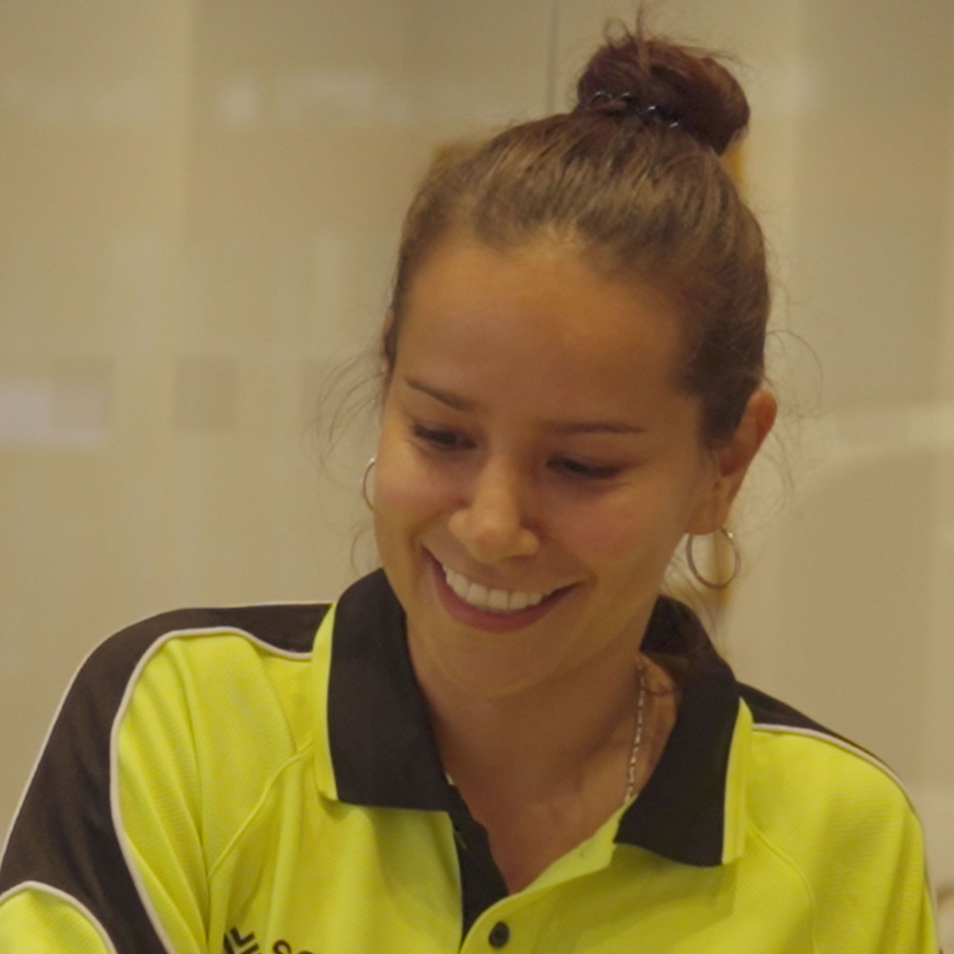 A woman wearing a yellow shirt with a black collar is smiling