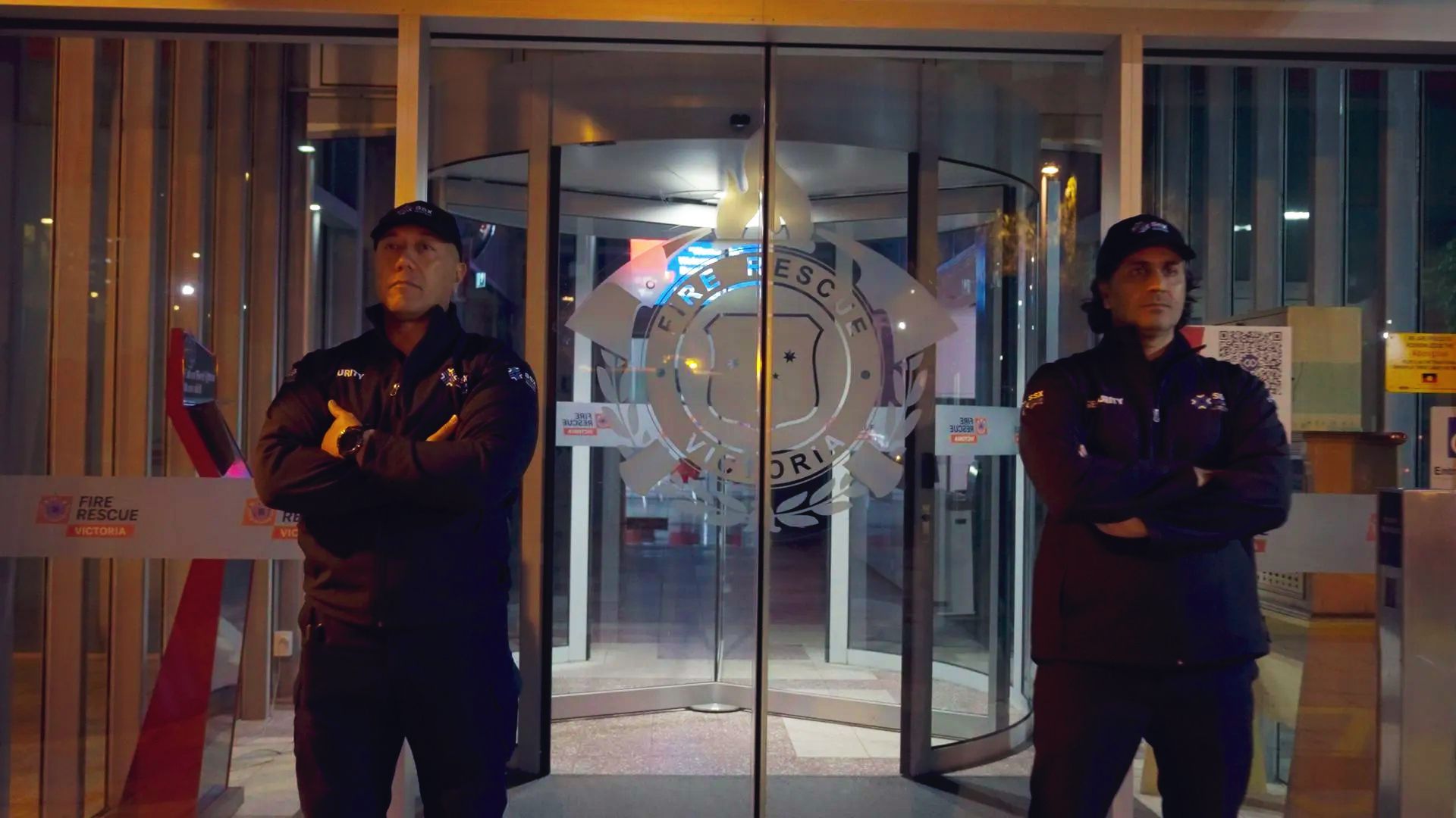 Two security guards are standing in front of a glass door.