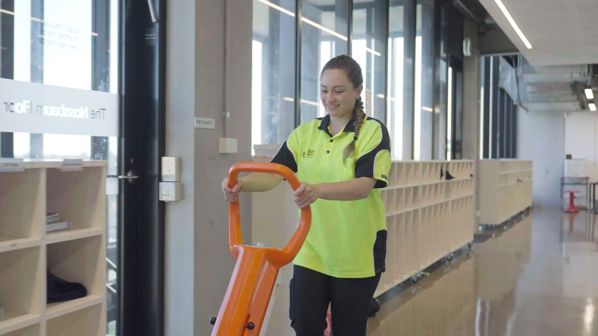A woman is pushing a cart down a hallway in a building.