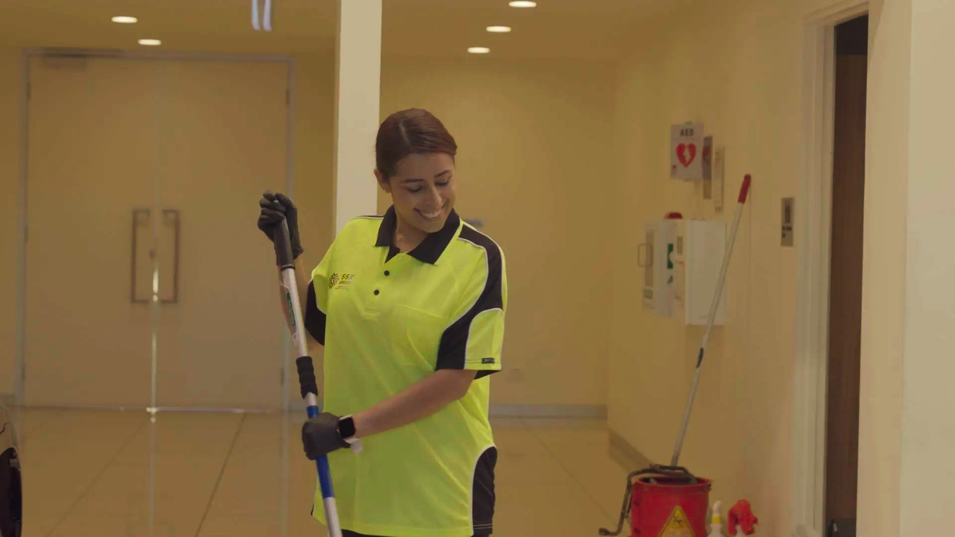 A woman is cleaning the floor with a mop in a hallway.