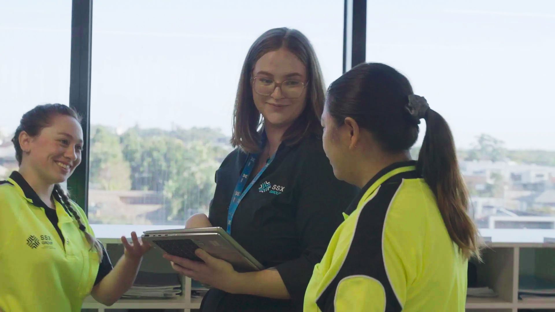 A group of women are standing next to each other in front of a window.
