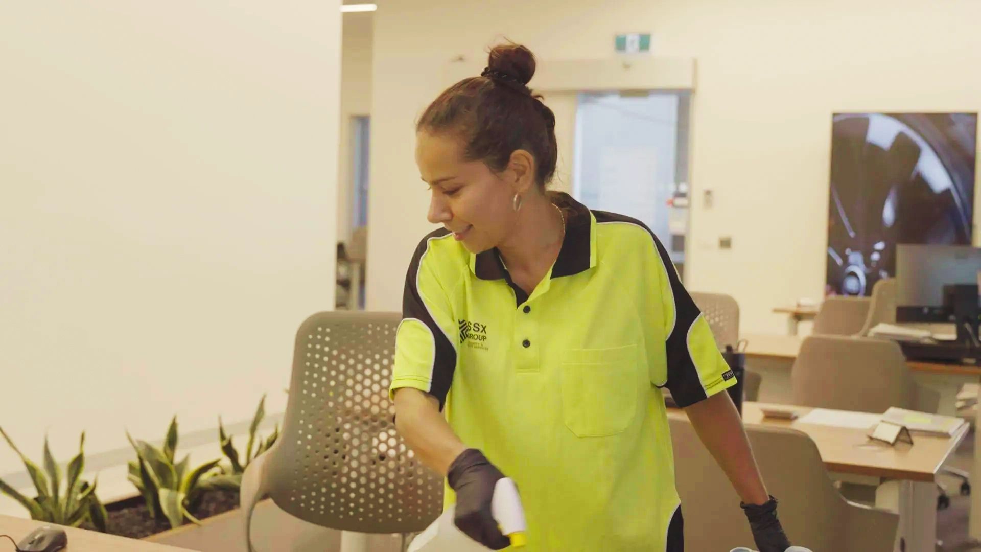 A woman is cleaning an office with a spray bottle.