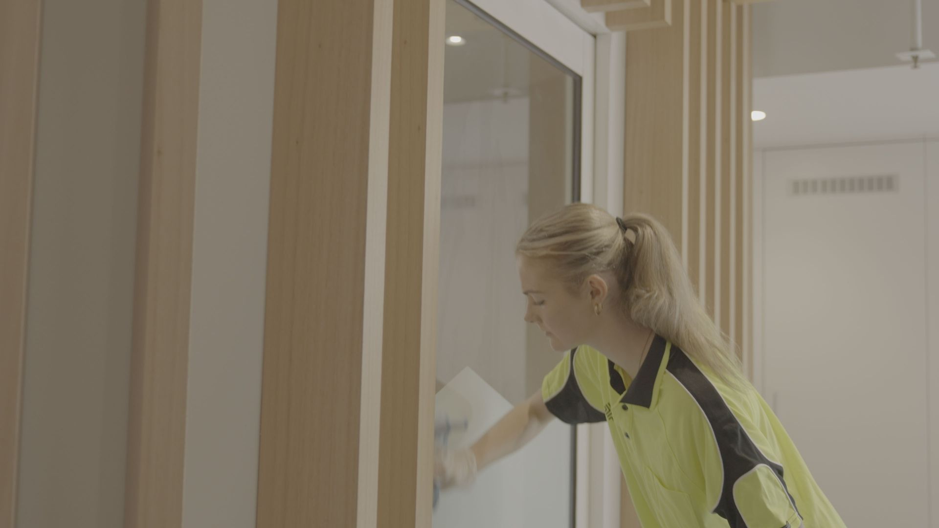A woman is cleaning a glass door with a cloth.