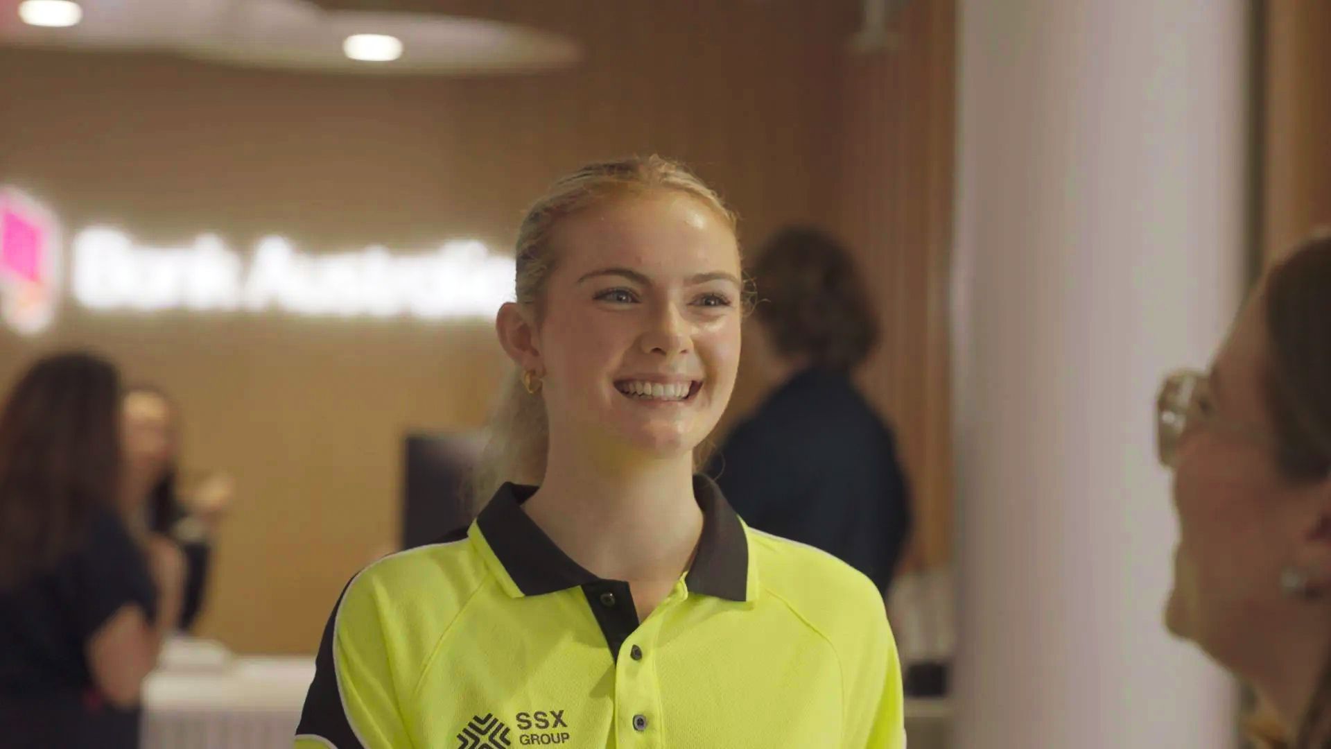 A woman in a yellow shirt is smiling and talking to another woman.