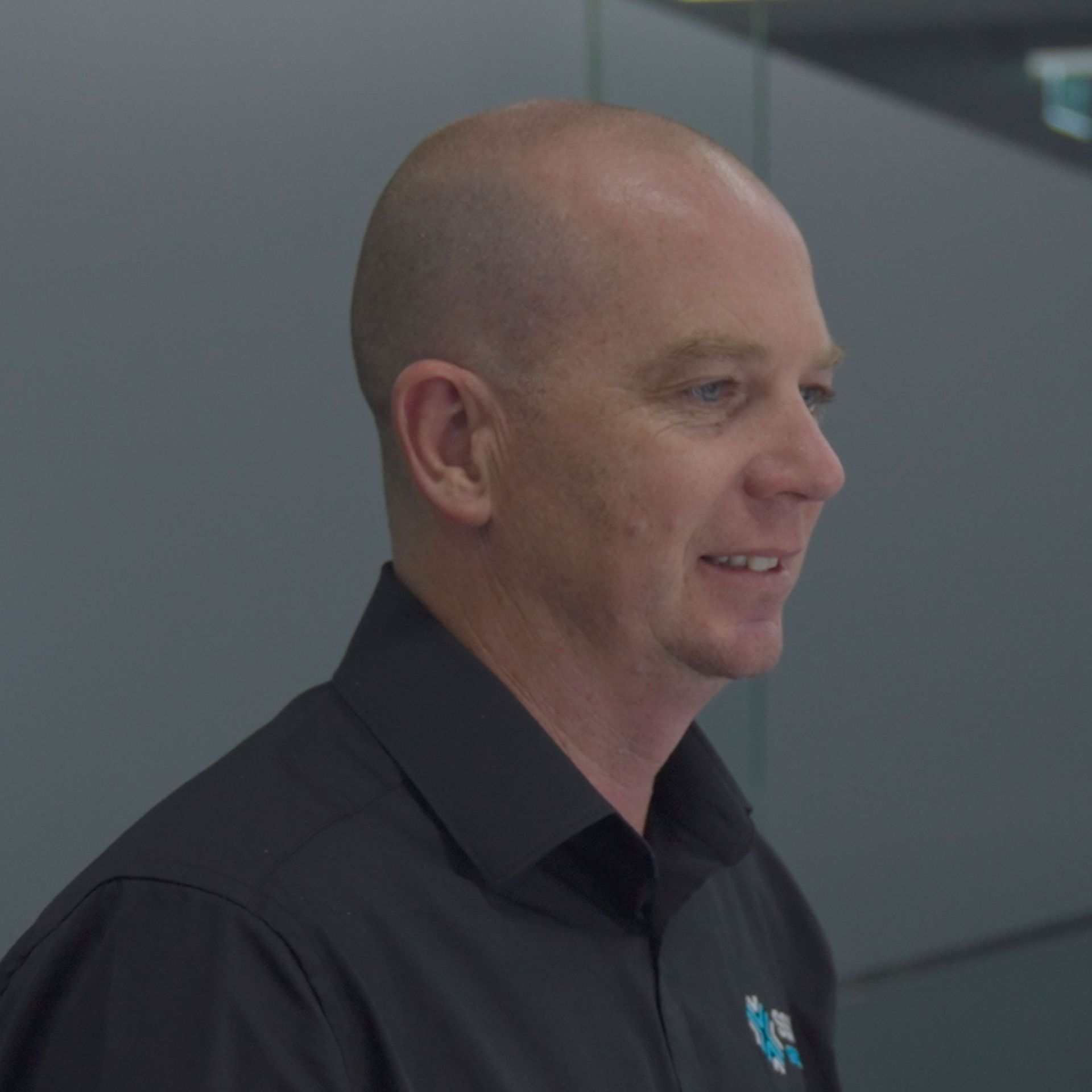 A man in a black shirt is smiling and looking to the side.