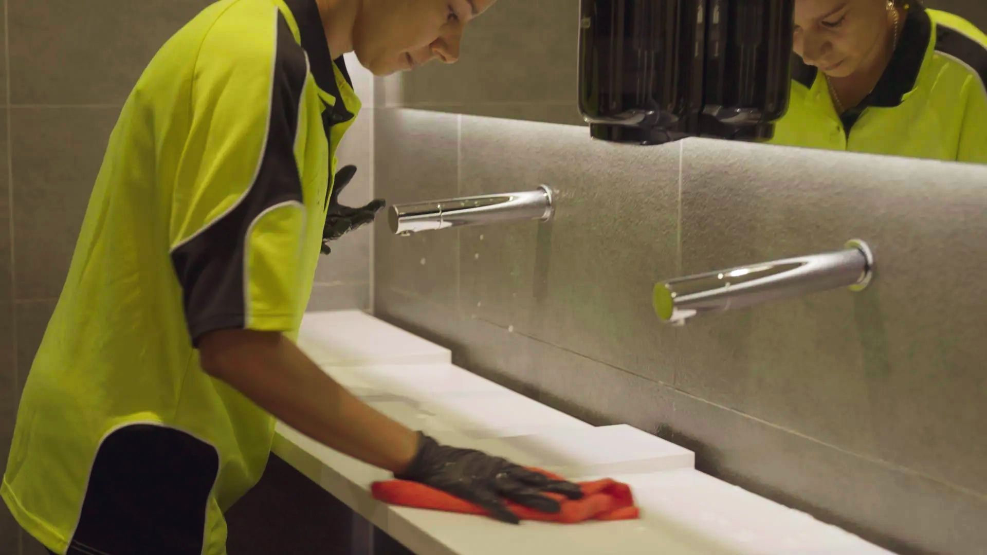 A man is cleaning a bathroom sink with a cloth.