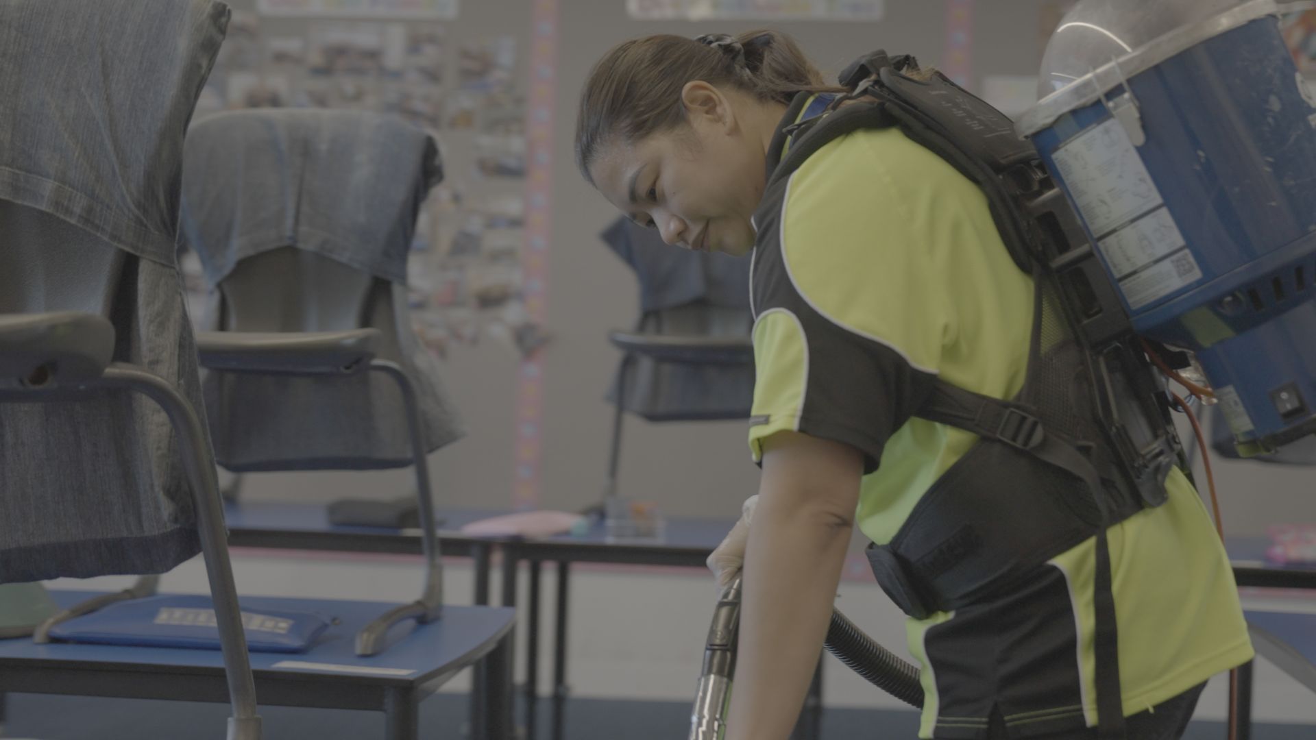 A woman is cleaning a classroom with a vacuum cleaner.