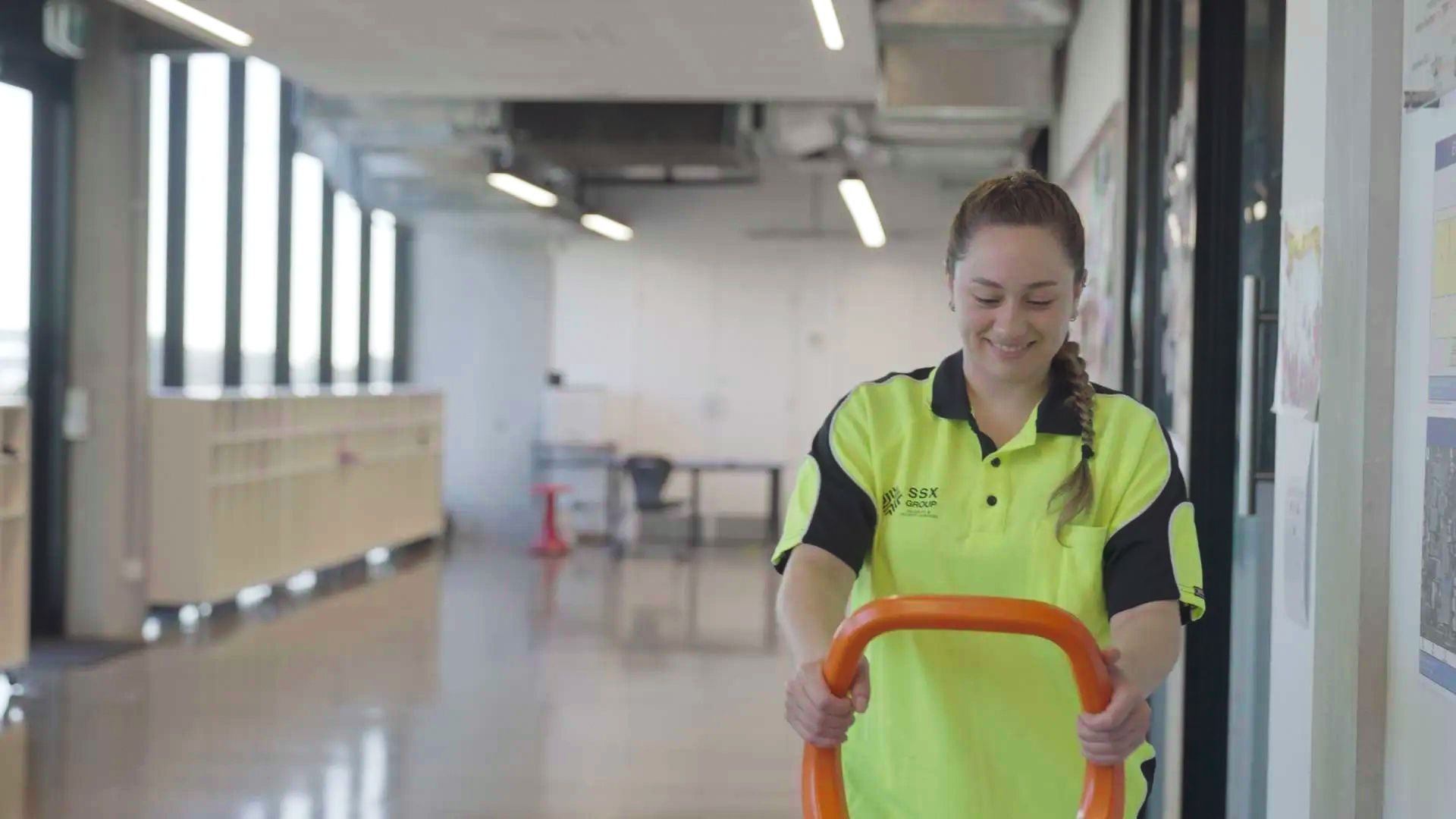 A woman in a yellow shirt is pushing a cart down a hallway.