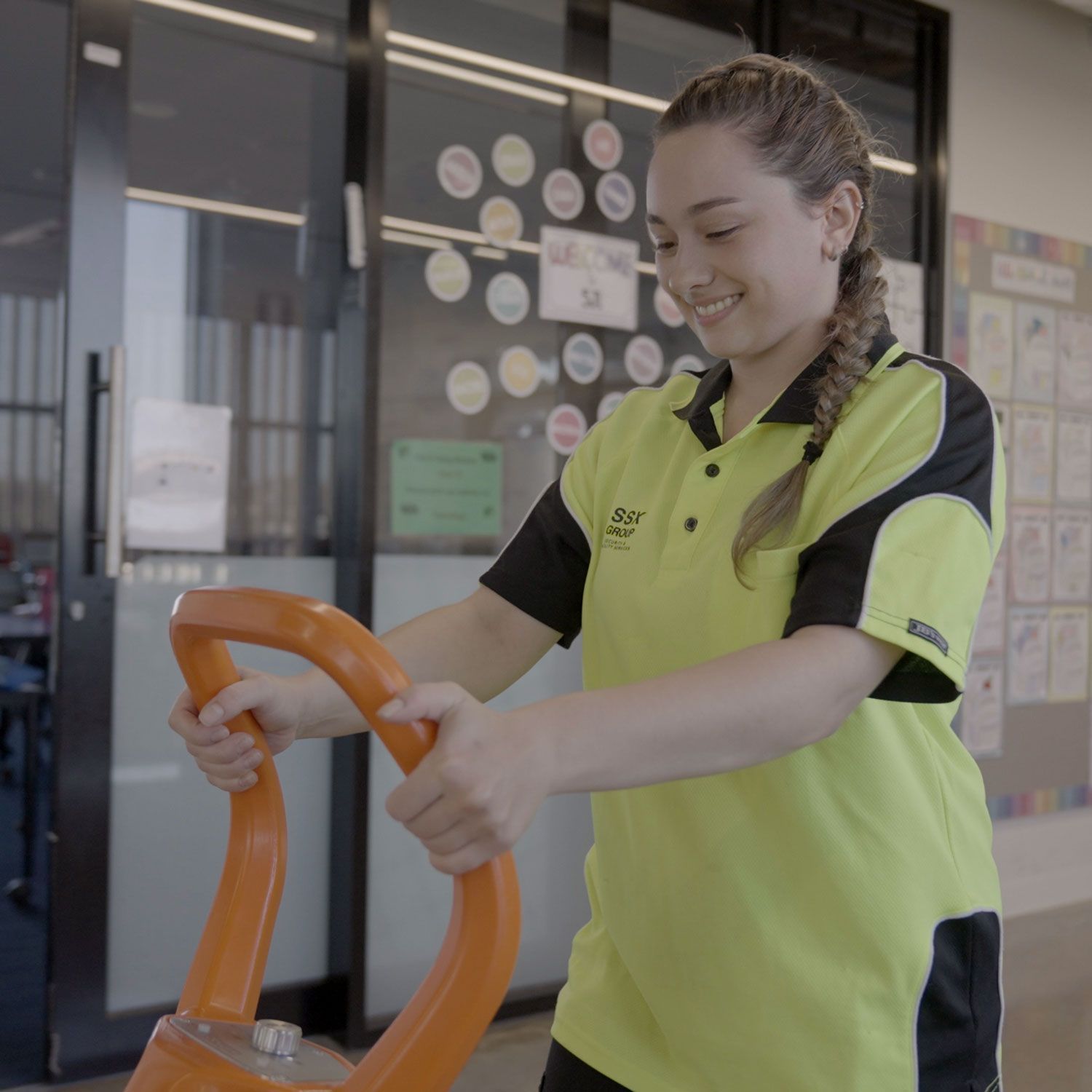 A woman in a yellow shirt is pushing an orange item