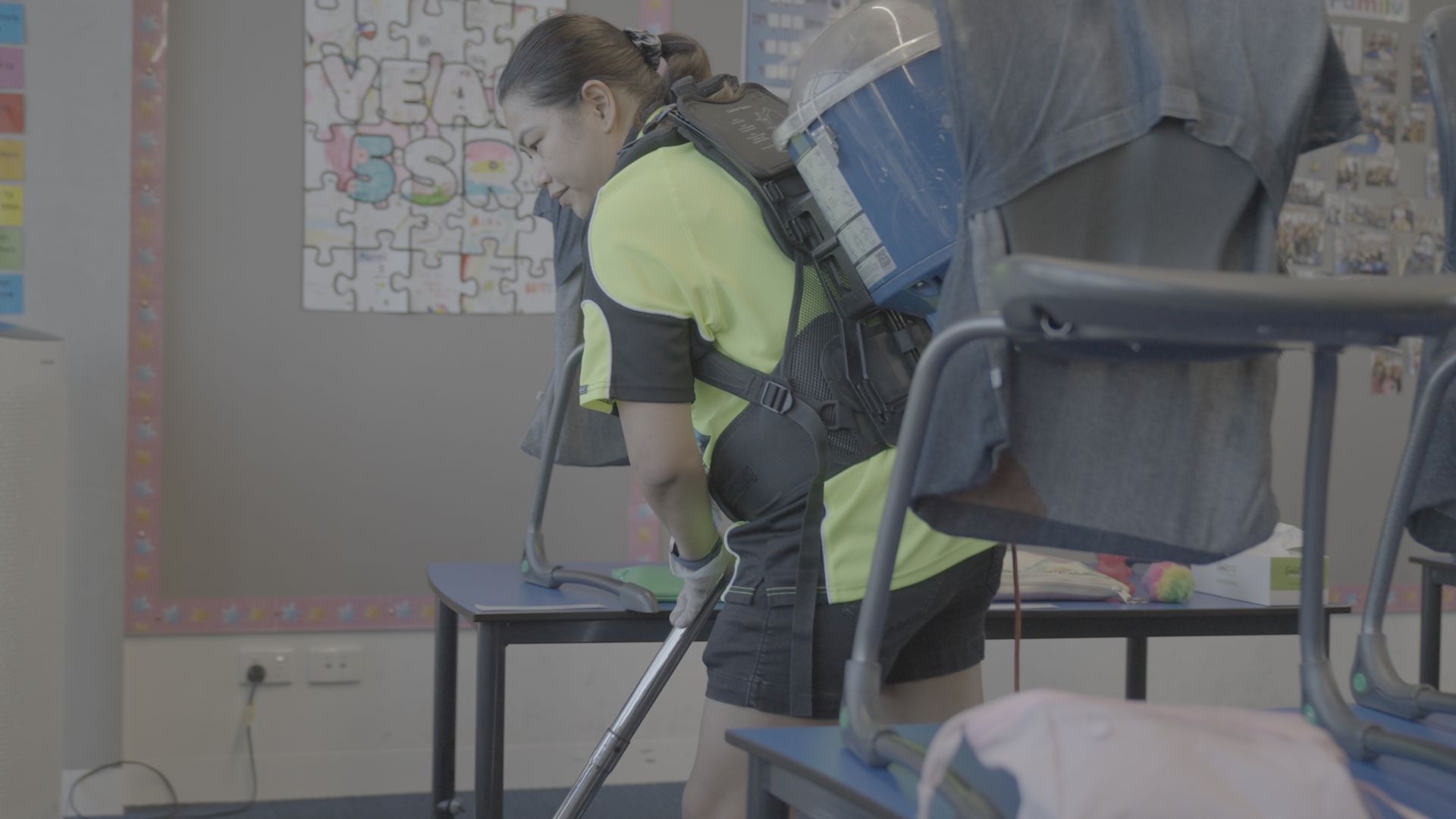 A woman is cleaning a classroom with a vacuum cleaner.