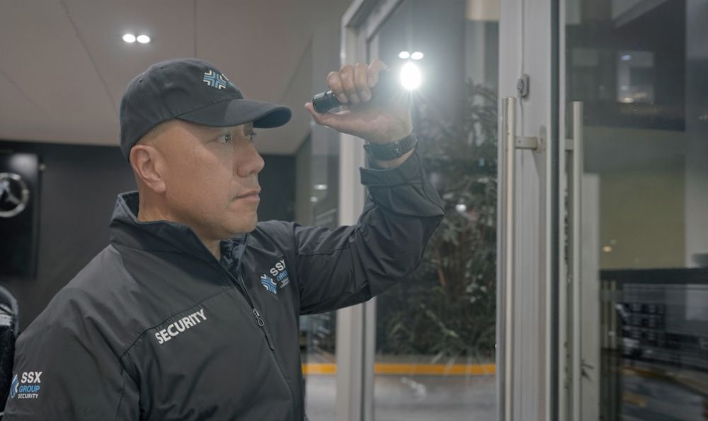 A security guard is looking through a glass door with a flashlight.