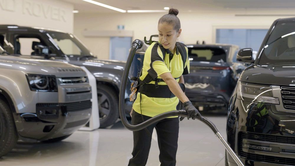 A woman is cleaning a car showroom with a vacuum cleaner.