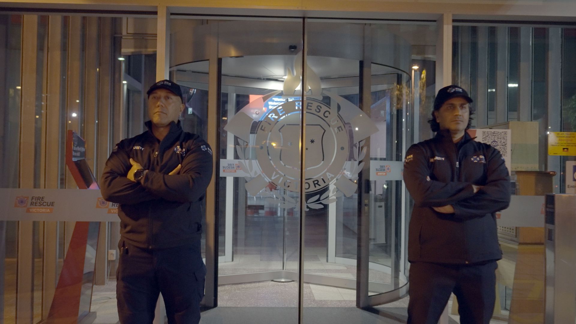 Two security guards are standing in front of a glass door.