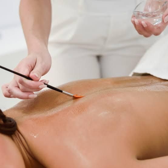 Persona recibiendo tratamiento de espalda, aplicando líquido con un cepillo en un entorno de spa.
