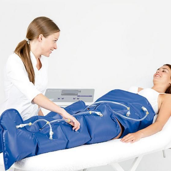 Mujer recibe terapia de compresión de piernas con un trabajador de la salud; vendajes azules, habitación blanca.