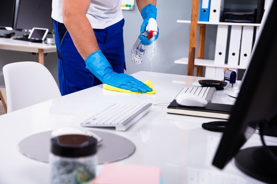 Cleaner Using Spray & Wipe On An Office Desk — Cleaning Services in Airlie Beach, QLD