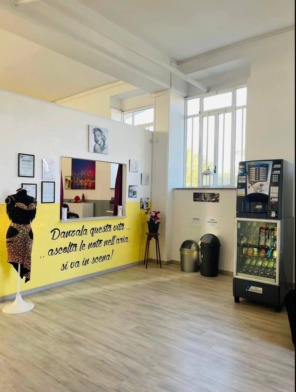Ripresa interna di uno studio con una parete gialla con del testo, un distributore automatico e un manichino che espone un indumento a fantasia.