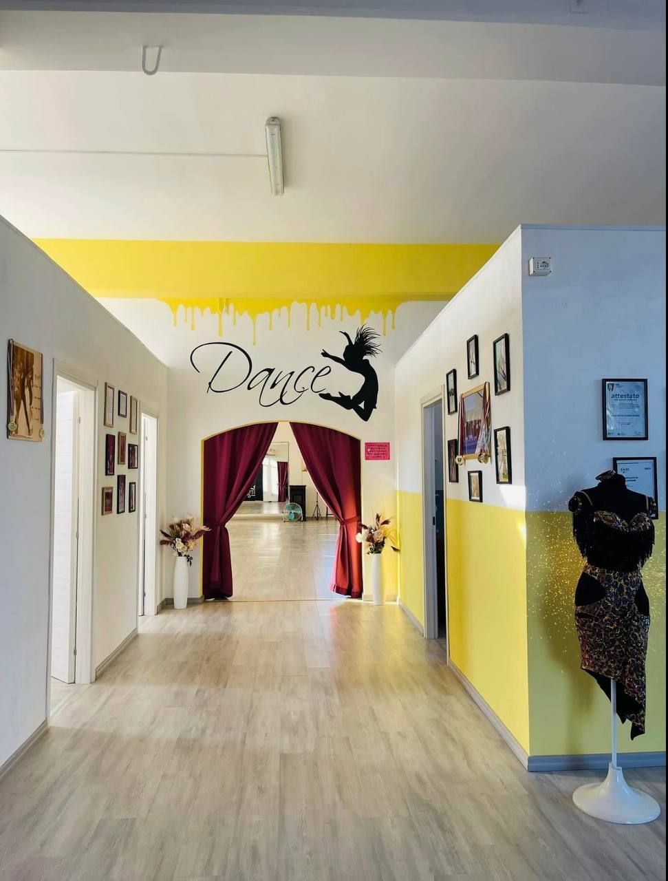 Corridoio di una scuola di danza con pareti gialle e bianche, tende color marrone e la scritta 
